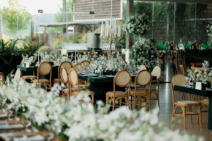 Elegant banquet hall decorated with white floral arrangements, candles, and black tablecloths, set for a formal event.
