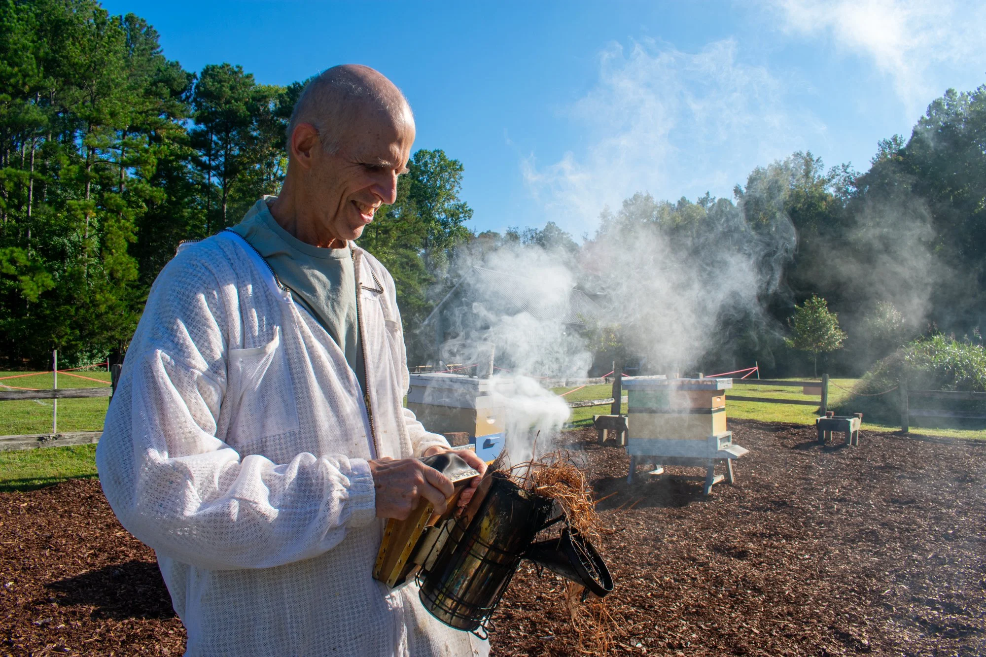 Brad Kosiba, beekeeper based in Hillsborough and a member of the OCBA, prepares to smoke a box hive by burning pine straw inside a fire chamber and puffing it repeatedly to catch a flame at Blackwood Farm Park in Orange County. He has been beekeeping