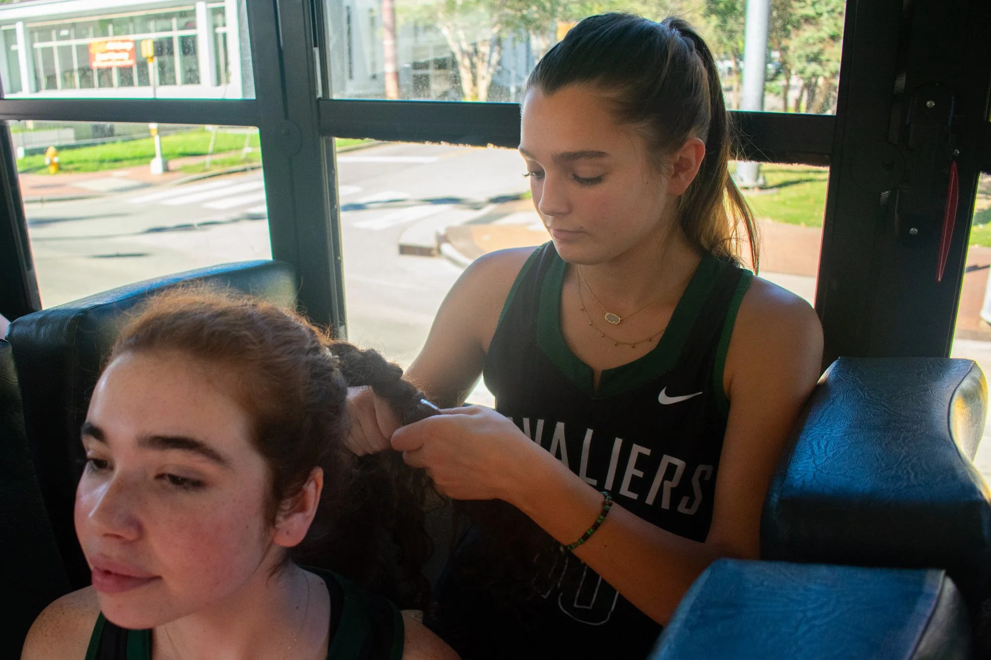 Siena Hurley braids Ali Vaccaro’s hair on the bus on the way to Saint Mary’s School. Before each game, the team captains lead stretches and warm-ups. The team chants a pregame hype song about the Cavaliers, Durham Academy's mascot. They also wear mat