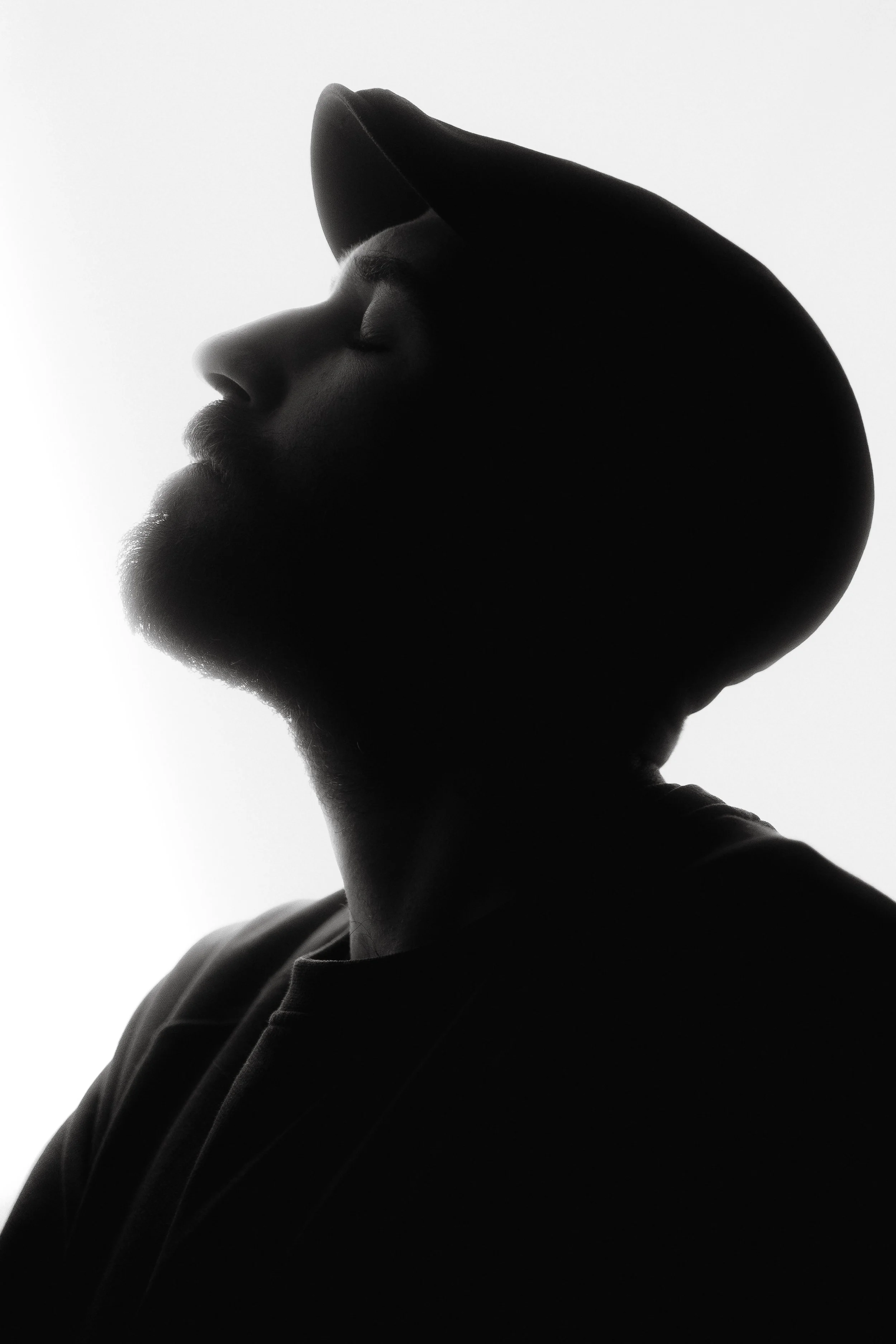 Black and white silhouette of a man wearing a hoodie with eyes closed, facing left, with a plain background.