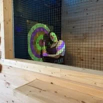 Person playing with a colorful tie-dye smiley face balloon inside an indoor play area with a wooden barrier.
