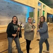 Three women standing together indoors, smiling and posing for the photo.
