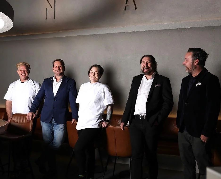 Five people, including chefs and restaurant staff, standing in a row and smiling in a restaurant setting.