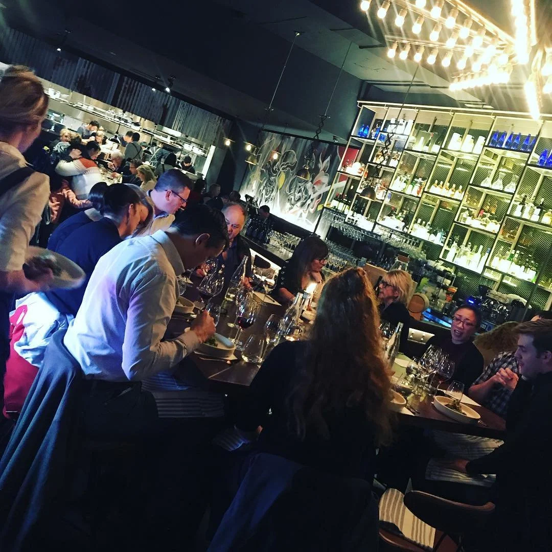 People dining at a busy restaurant with a bar and modern decor.