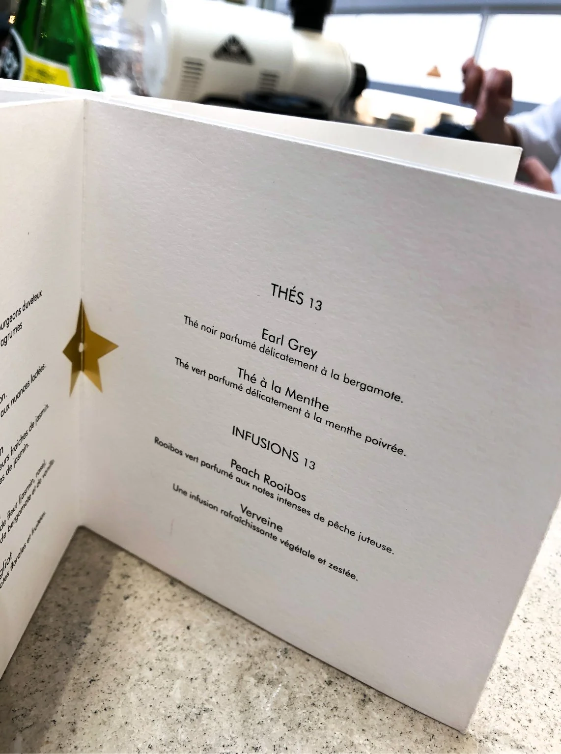 Close-up of a tea menu with options for Earl Grey and mint tea, and infusions like peach rooibos and verbena, on a table.