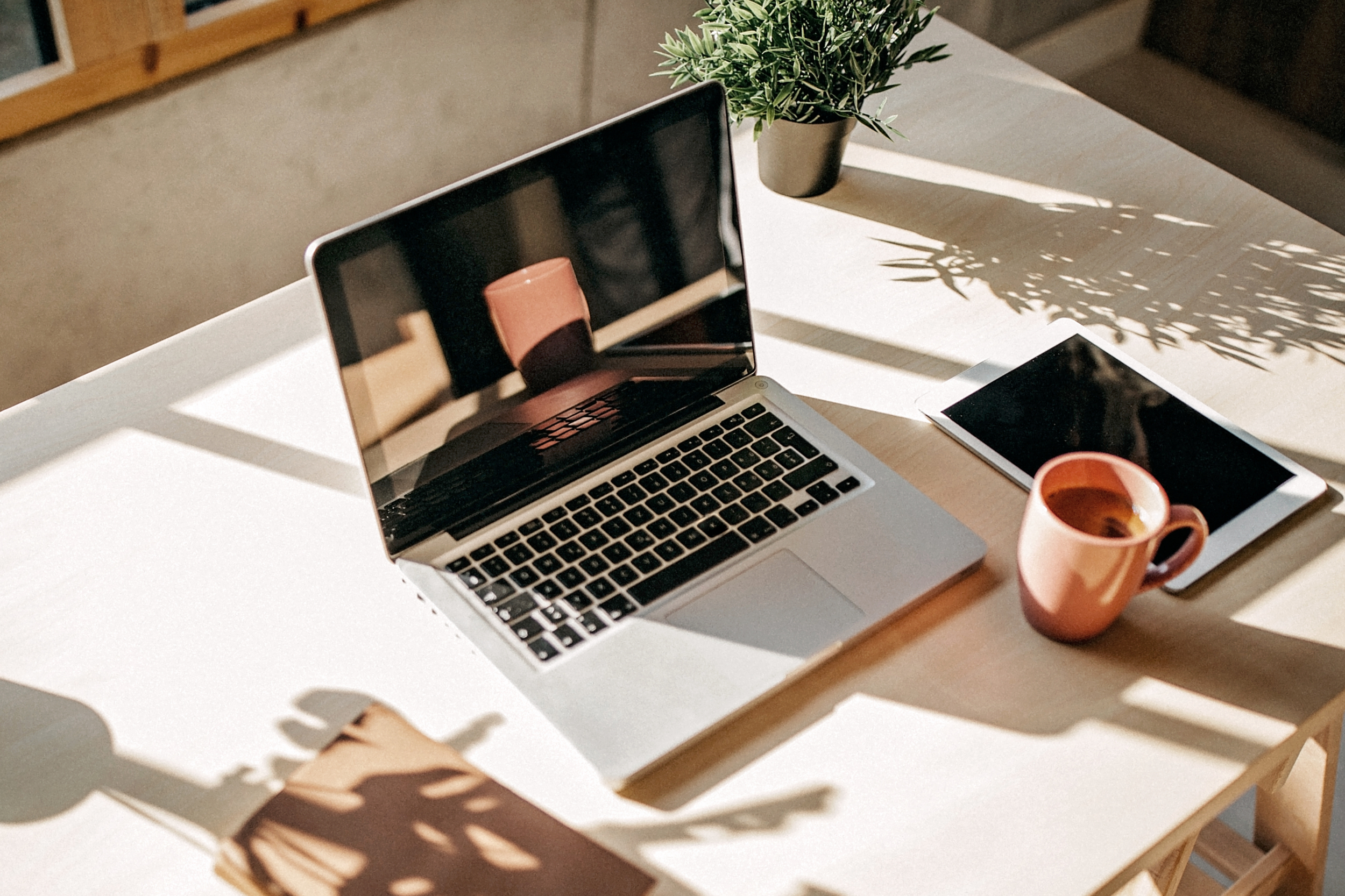 Sunlit therapy office desk with laptop, tablet, coffee mug, and plant at Meadowbrook Counseling in Athens, Alabama.