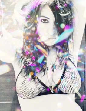 A woman with dark hair, winking at the camera, surrounded by colorful light reflections and bokeh effects.