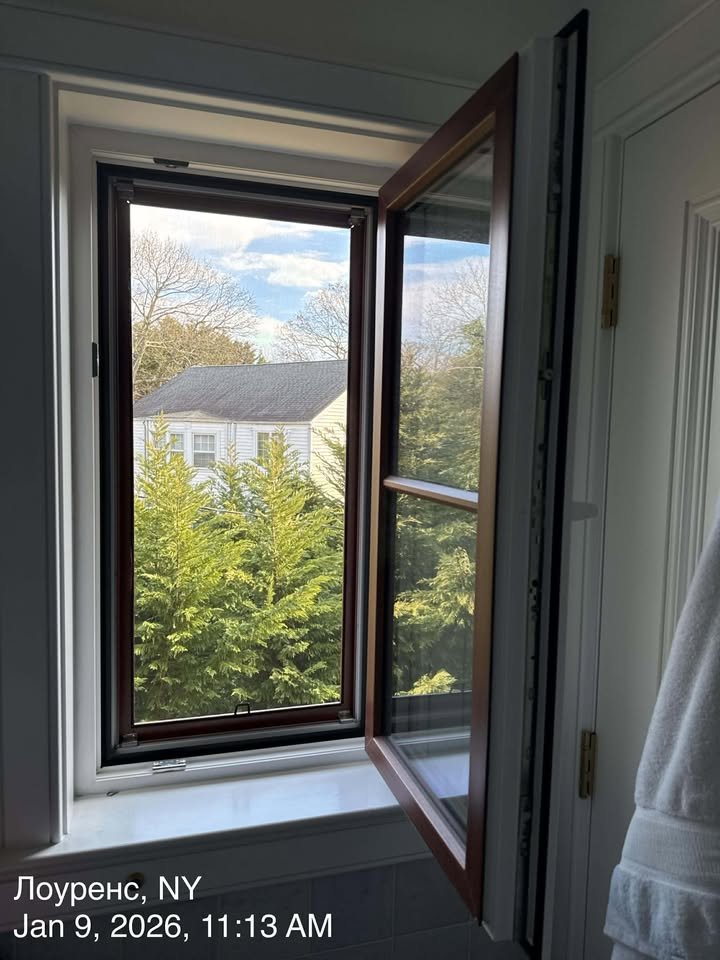 Open window in a house showing trees and a neighboring house outside on a clear day.
