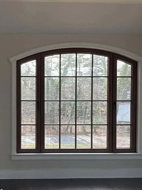 Large arched window with multiple panes in a house, view of trees and a driveway outside.