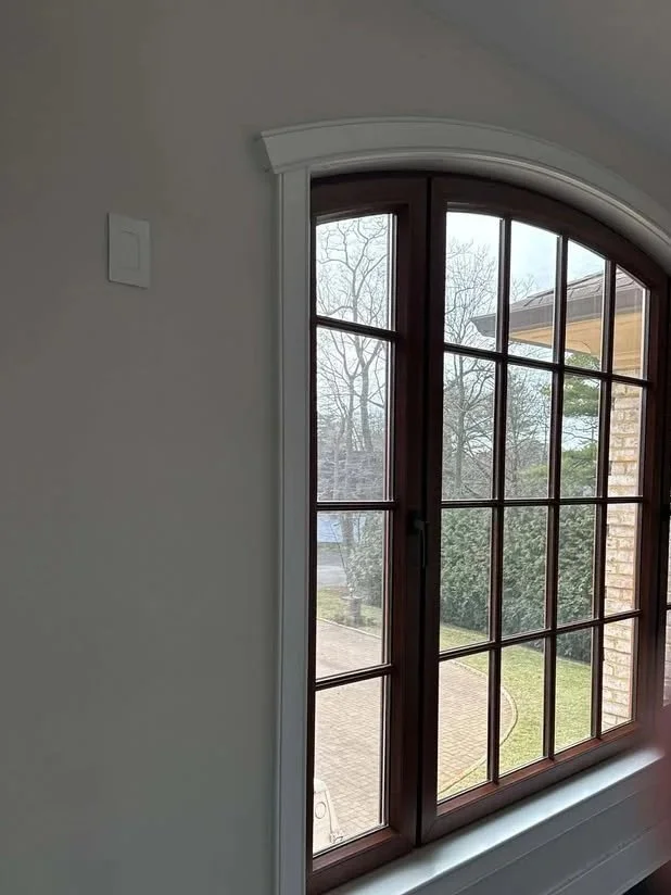 View through a large arched window showing trees and part of a brick house exterior