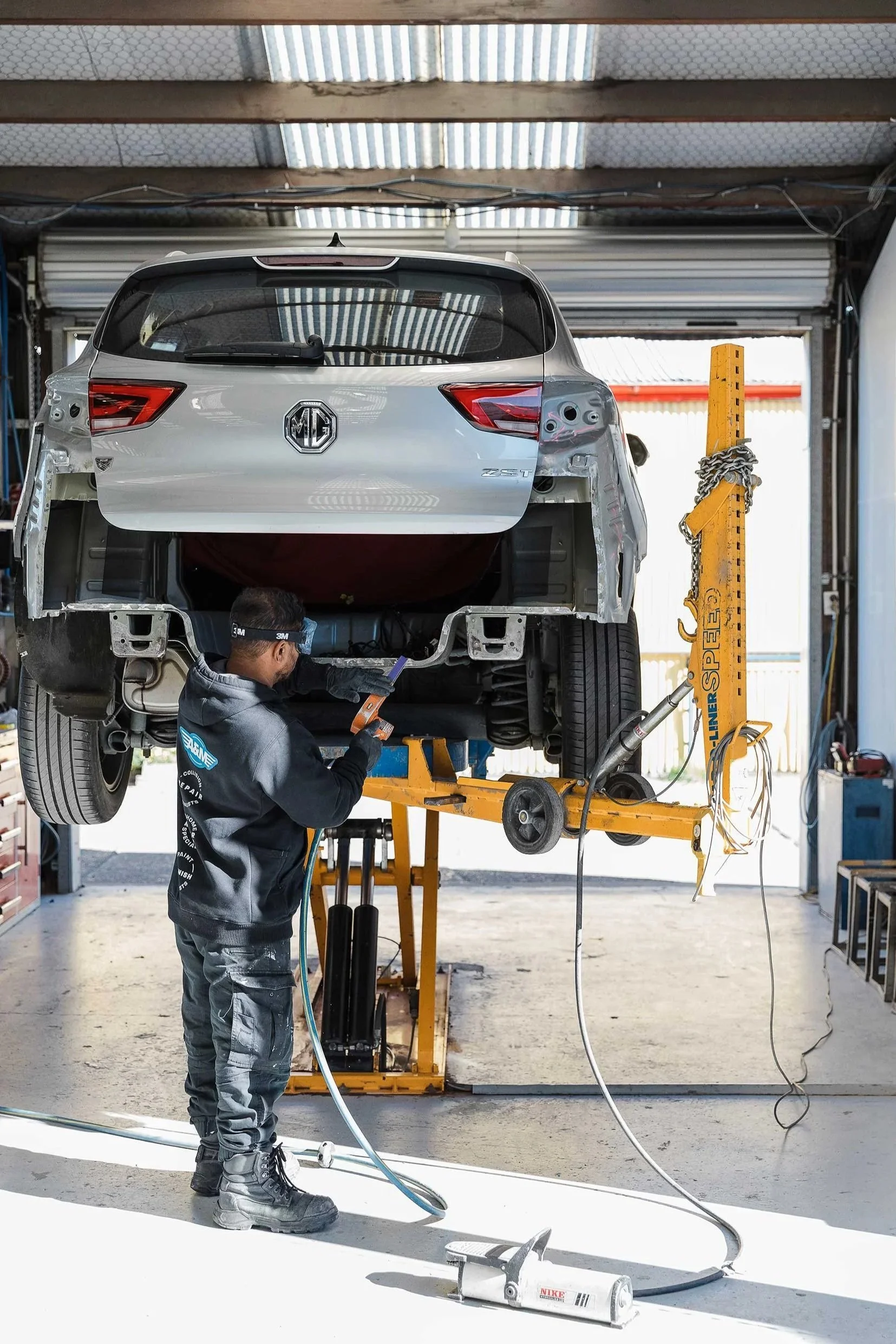 A&M Panel Repair team member works underneath a crash damaged car that is elevated on a hydraulic lift in the Napier workshop.