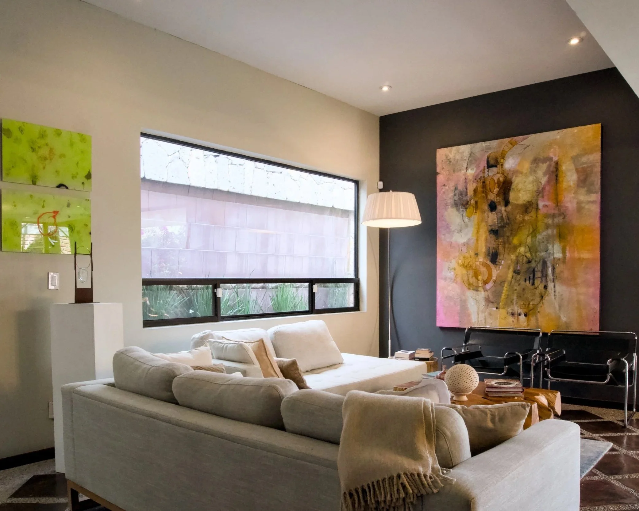 Modern living room with white sofa, large window, abstract artwork, floor lamp, and black chairs.