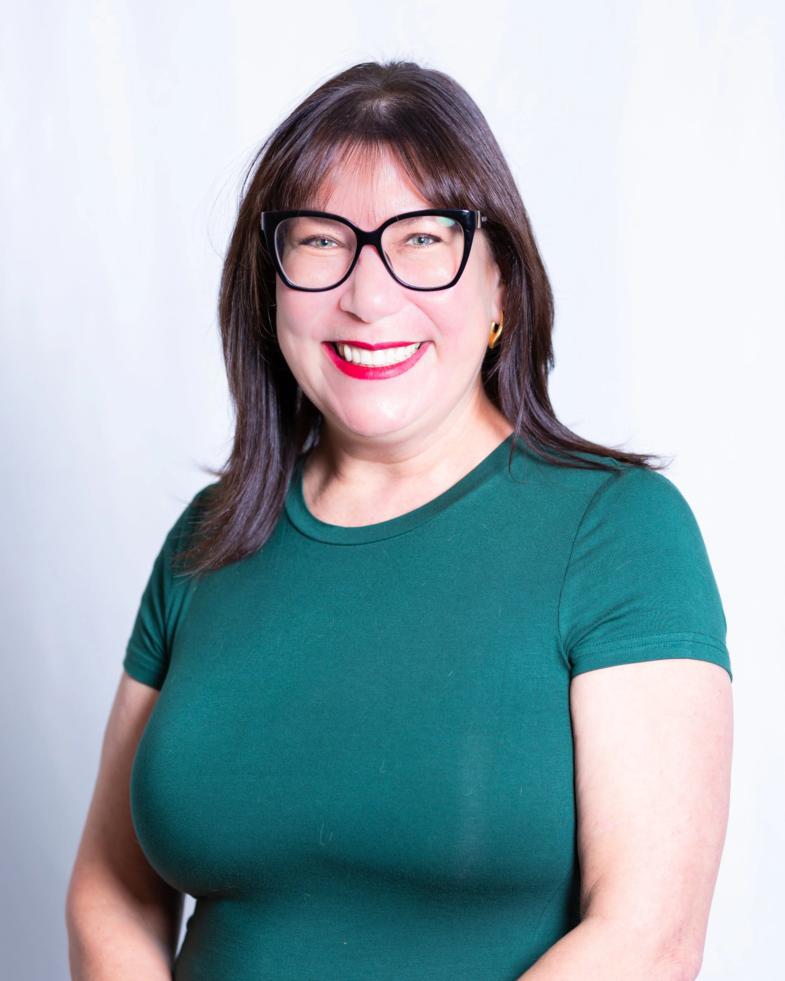 A woman with dark brown hair wearing glasses, a green t-shirt, and red lipstick, smiling.
