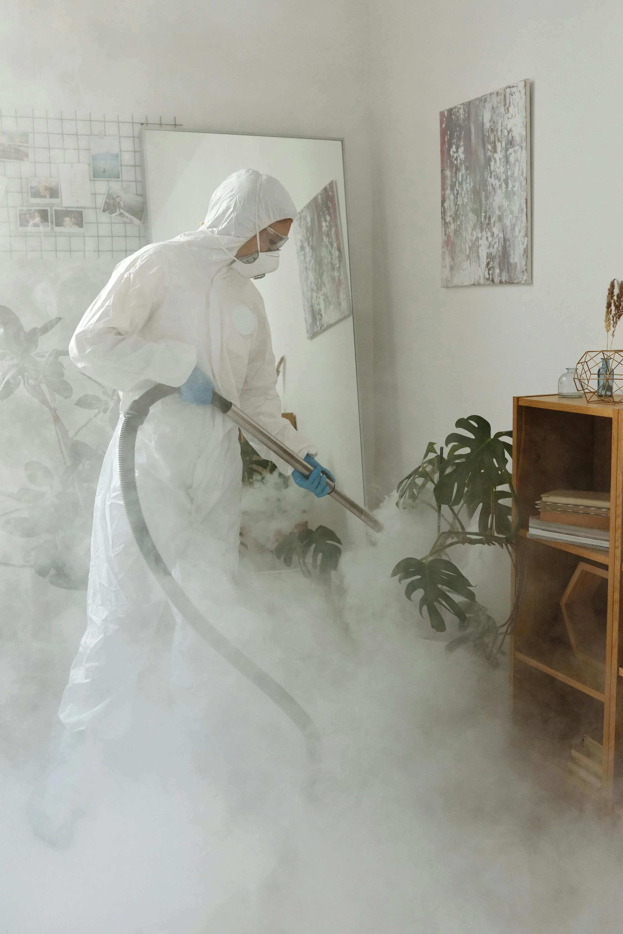Person in protective suit and mask using fogging machine to disinfect a room filled with fog or vapor.
