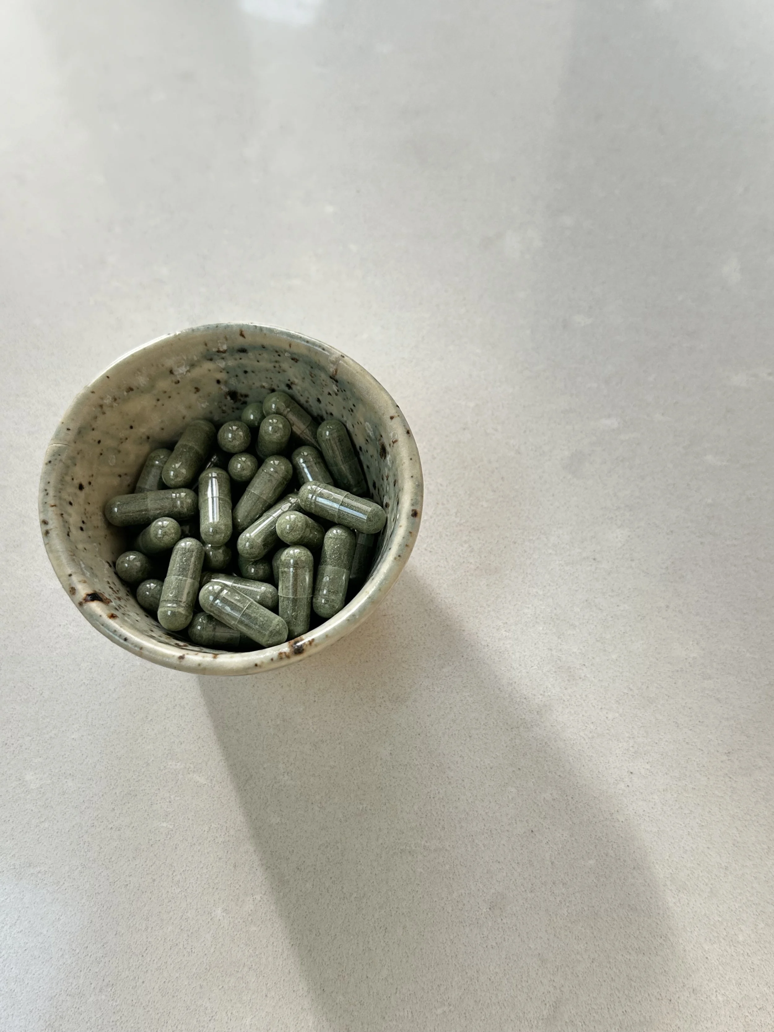 A small ceramic bowl filled with green capsules on a white surface.