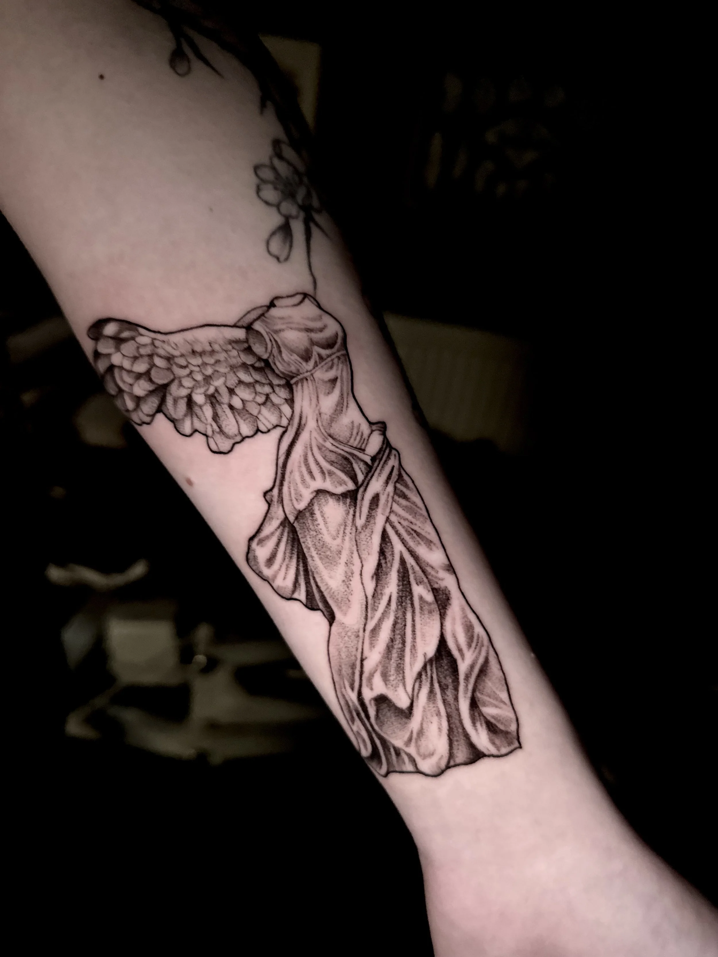Black and gray tattoo of a fairy with butterfly wings on a person's forearm.