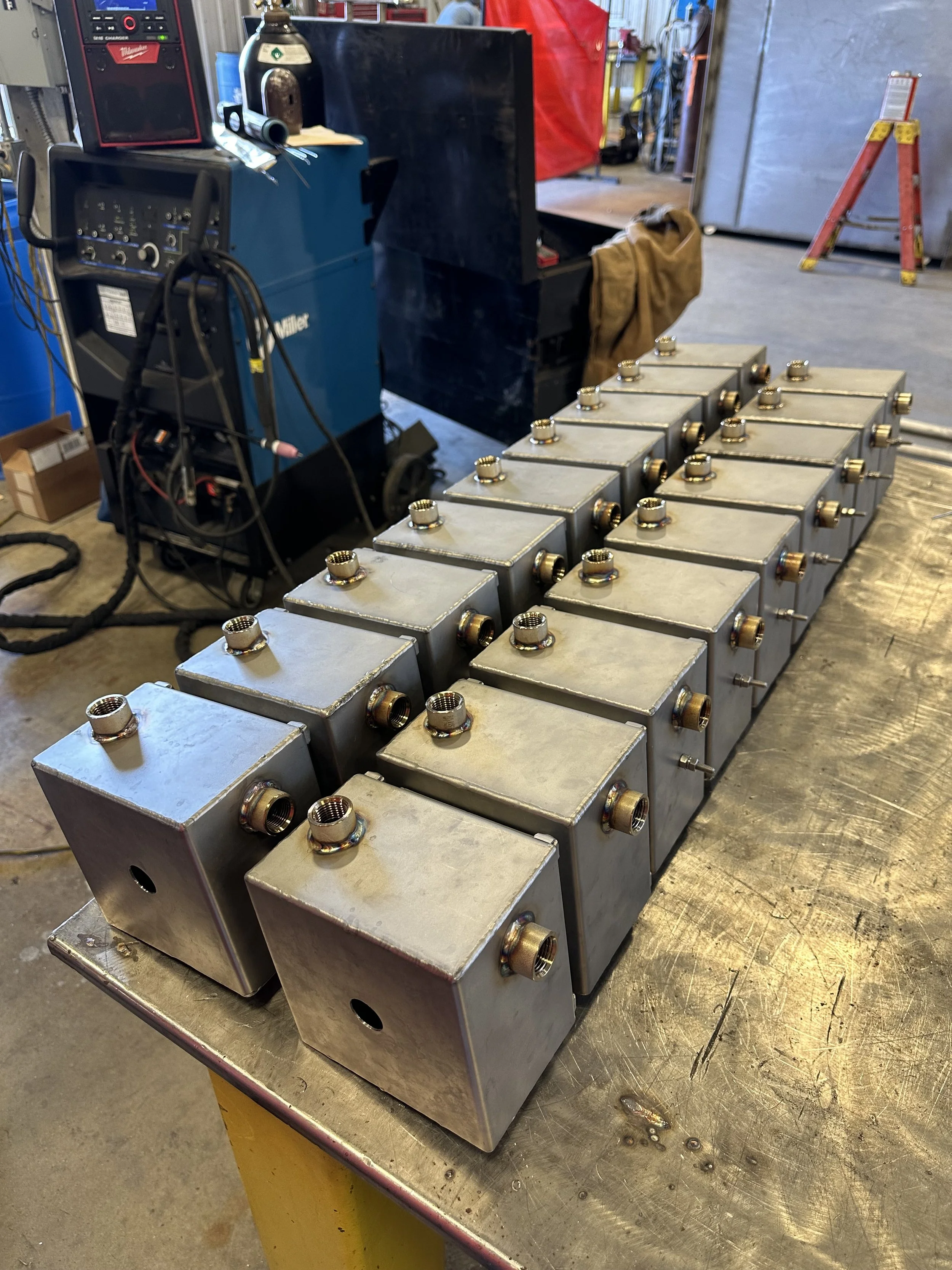 Multiple metal boxes with threaded connectors on a workbench in a workshop setting.