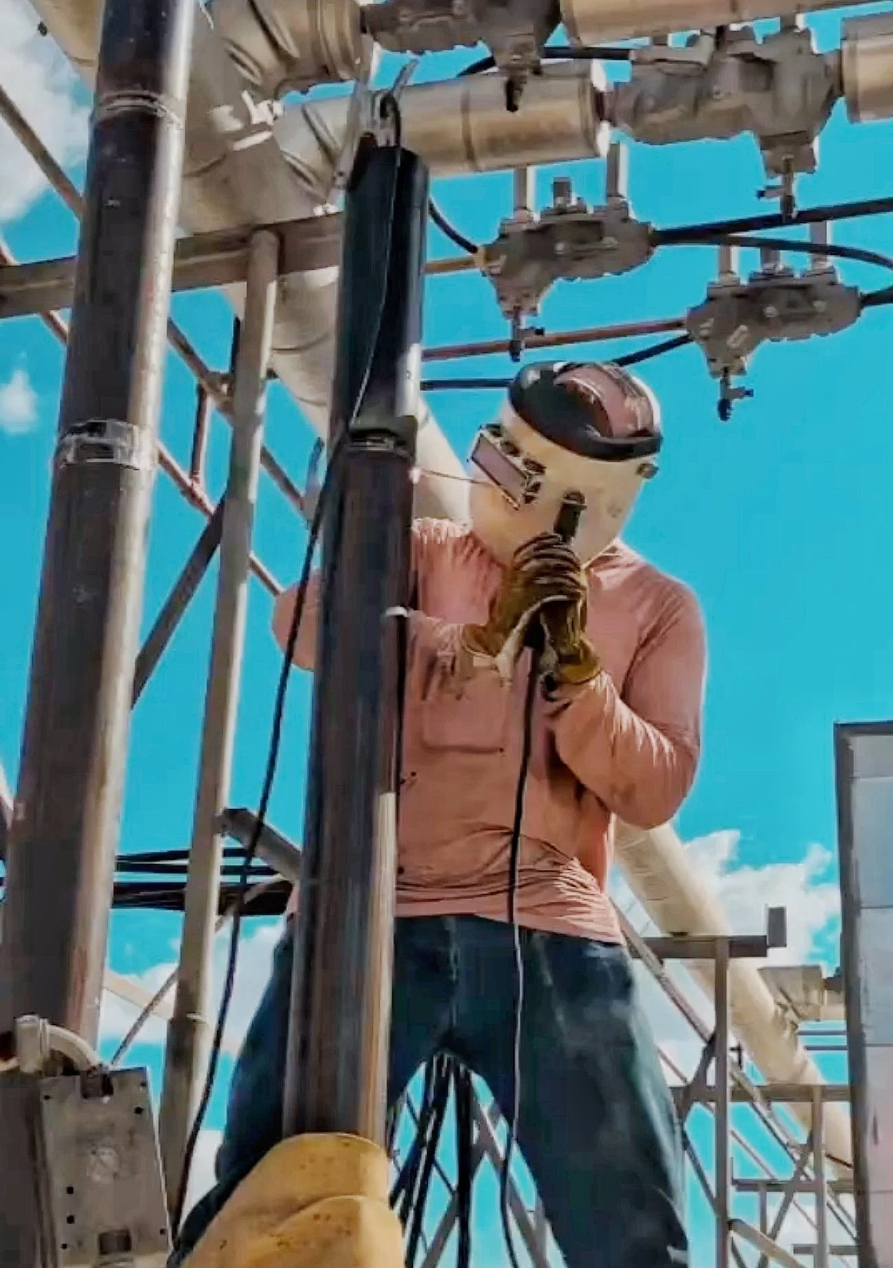 A worker installing or repairing equipment on an outdoor electrical tower against a blue sky with some clouds.