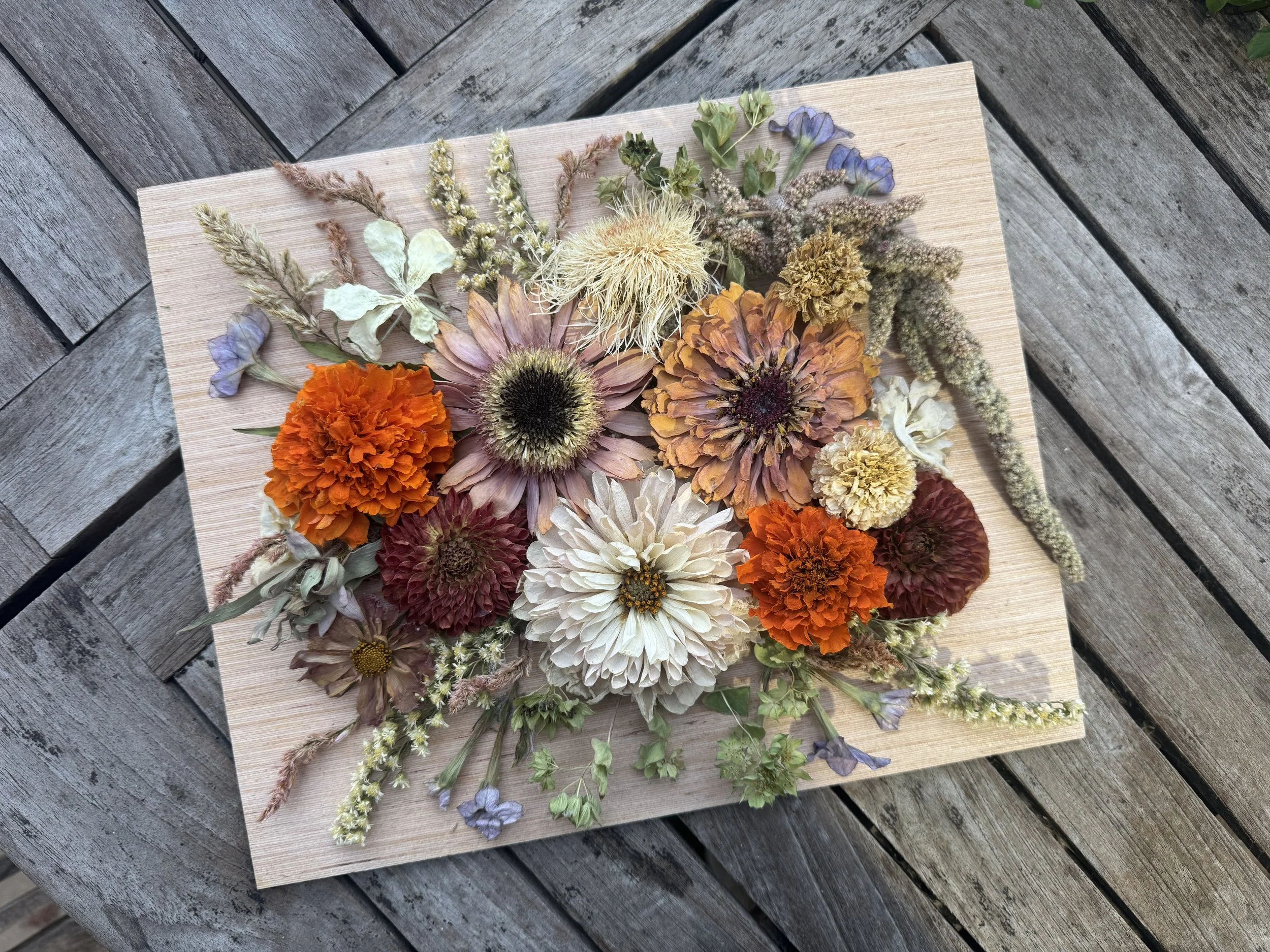 A wooden surface with a variety of dried flowers arranged on top, including orange, white, purple, and beige blooms.