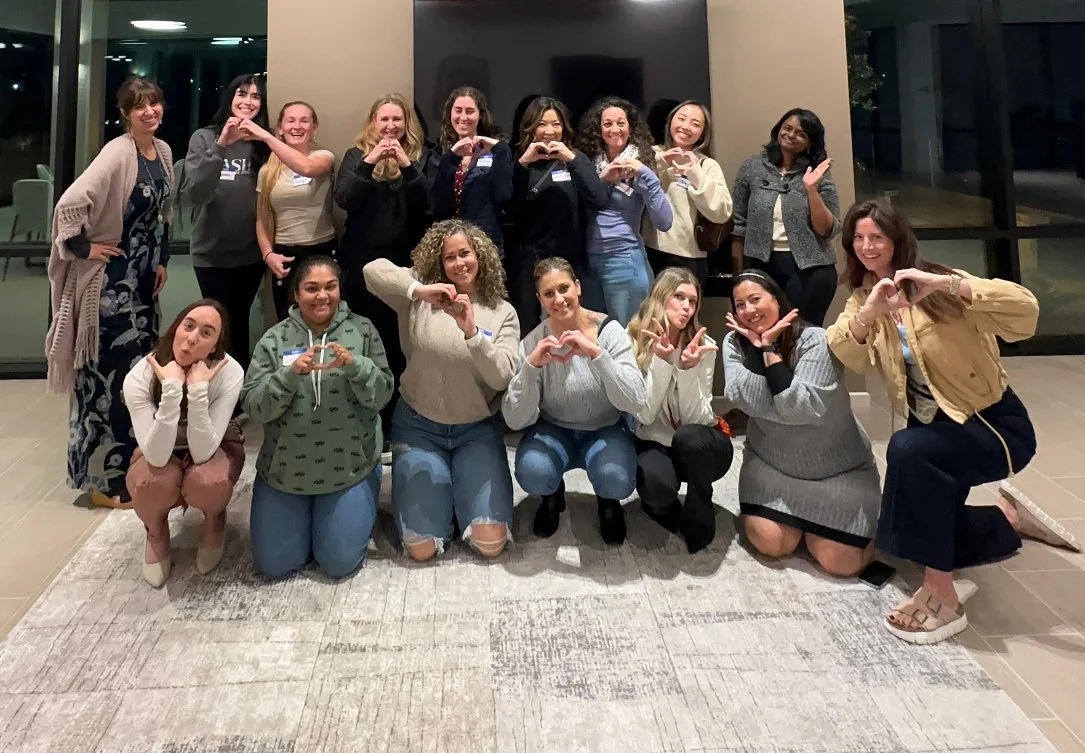 LetsGoGirls San Diego posing together indoors, many making heart shapes with their hands. The setting suggests a friendly, empowering, and community-focused gathering.