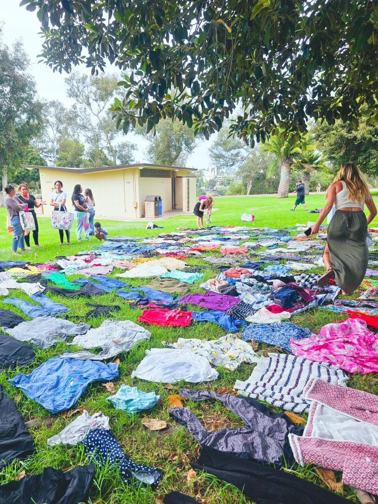 LetsGoGirls San Diego Clothing Swap event featuring members exchanging clothes outdoors in a park setting, with colorful clothing displayed on the grass for a sustainable fashion community gathering focused on connection and sharing.