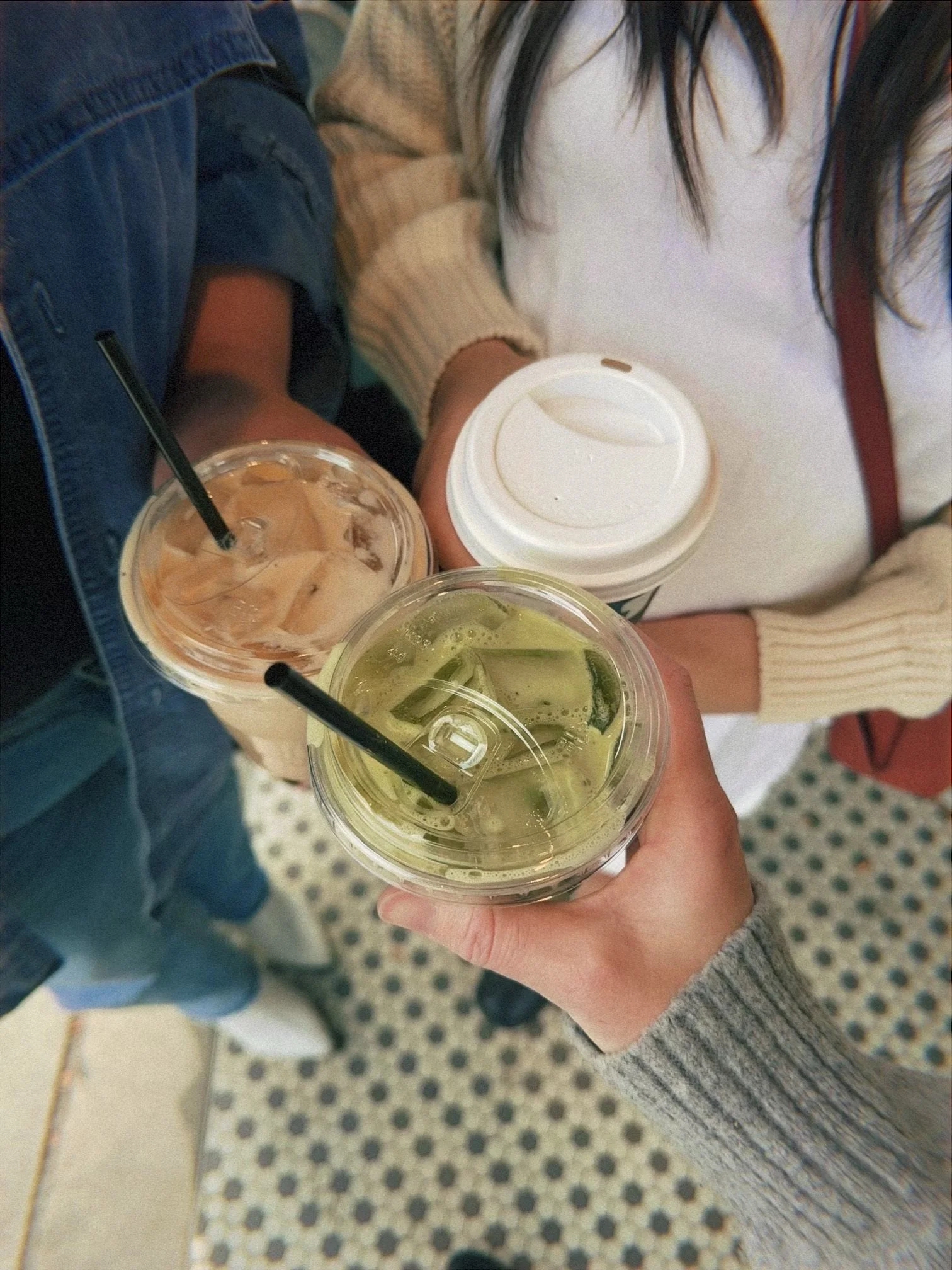 Three people holding different drinks — one iced coffee, one iced matcha, and one hot coffee — clinking their cups together, capturing a moment of friendship and casual enjoyment.