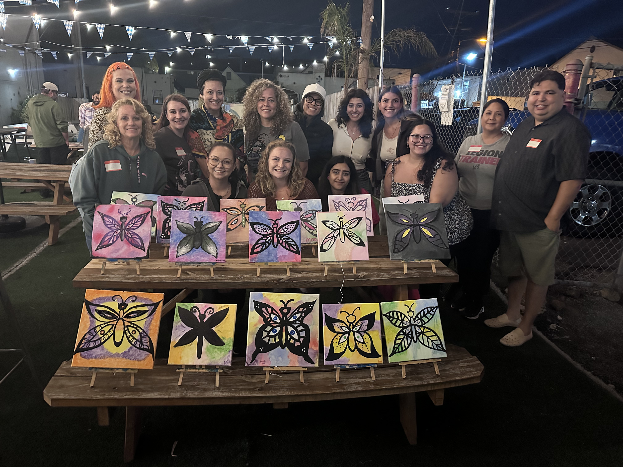 A group of participants from a 'Let's Go Girls' event in San Diego, proudly displaying their butterfly artwork after a painting activity. The photo captures the creativity and connection among the women at the event.