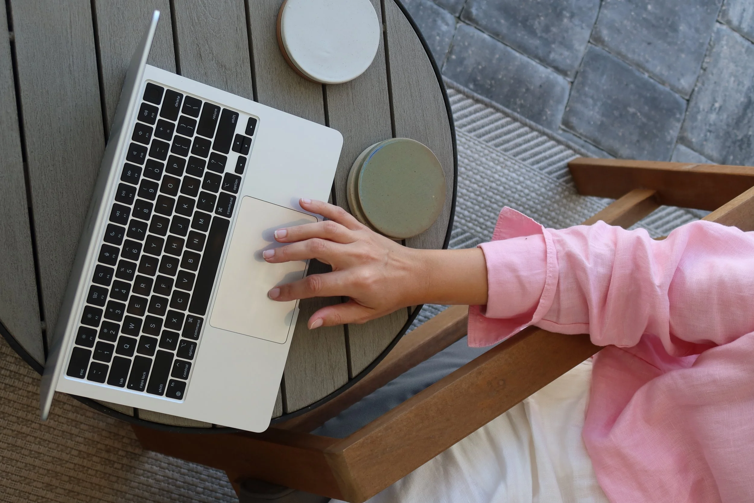 Minimal outdoor workspace with a laptop on a round table, featuring a person working from a patio setting with a coffee cup, representing productivity, remote work, creativity, and modern entrepreneurship.