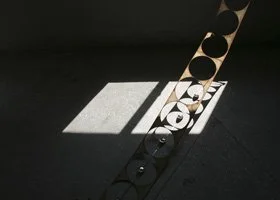 Sunlight casting shadows through a round hole in a metal strip onto a floor, creating circular patterns.