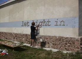 Two children standing in front of a wall with the words 'left right in' written on it, painting or writing on the wall.