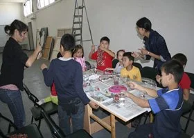 Children gathered around a table making arts and crafts with two adults supervising.