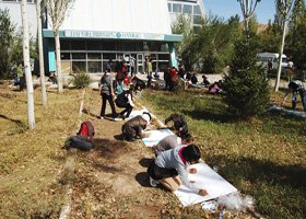 People planting trees in an outdoor area near a building, with some watching and others actively planting.