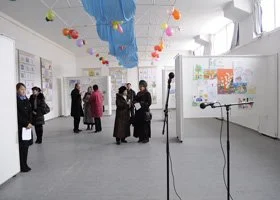 People viewing art displays in an indoor art exhibition with colorful hanging decorations.