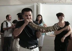 A man in a black shirt is holding a large snake in an indoor setting, with other people in the background.