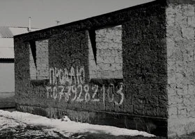 Black and white photo of a brick building with large painted text on the wall.