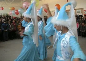 Group of women in blue traditional costumes and cone-shaped hats performing a dance in a crowded room.