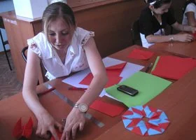 Girl making paper craft at a table with red and green paper and a smartphone