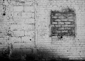 Black and white photo of a brick wall with a square opening or window and some graffiti or markings.