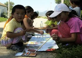 Children painting outdoors on a large canvas laid on the ground.