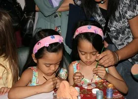 Two young girls with pink headbands decorating cookies at a table during a party.