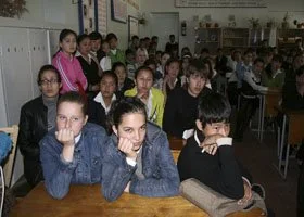 Students sitting at desks in a classroom, some looking forward and some writing or reading.