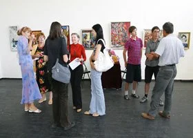 People attending an art gallery, viewing paintings and engaging in conversation.