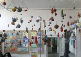 Children's art exhibition with colorful hanging decorations and artwork on display in a bright room.