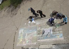 A group of people painting a large colorful mural on the ground