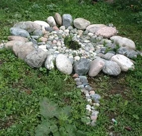 A garden decoration resembling a cross, made of various sized stones and pebbles, placed on grass.