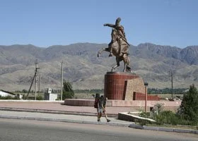 Statue of a cowboy on horseback on a brick pedestal in an open area with mountains in the background