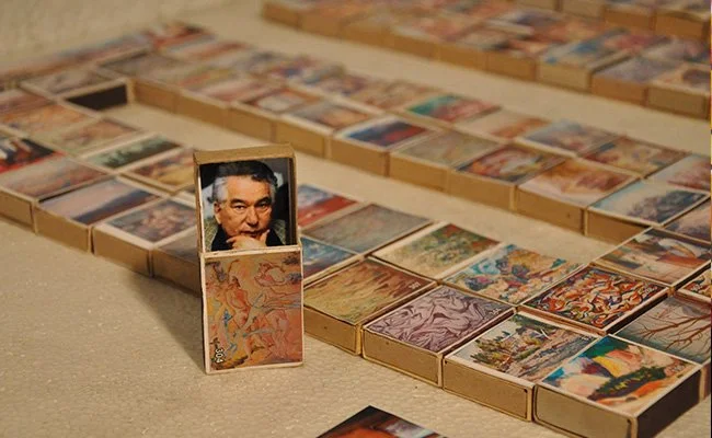 A collection of matchbox-sized boxes arranged on the floor, with a matchbox featuring a man's face placed vertically among them.
