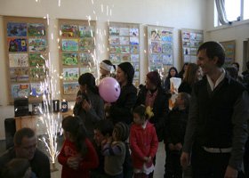 Group of children and adults in a room with colorful artwork displayed on the walls, celebrating with a pink balloon and sparklers.