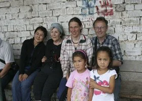 Six people, including two children, standing and sitting in front of a white brick wall.