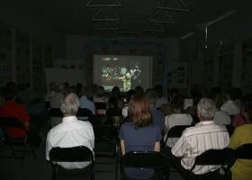 People seated in a dark room watching a presentation or film projected on a large screen.